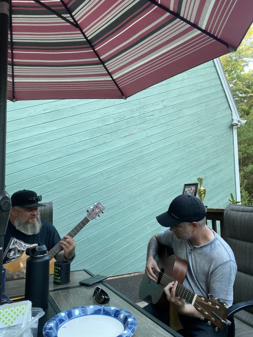 Ran Kime and Terry Bouchie playing acoustic guitars on outdoor deck