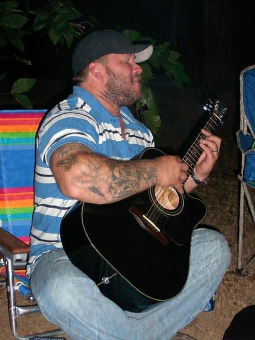 Ran Kime of dirty lil’ trollops playing guitar by a campfire, where late-night jams and loose ideas turned into lasting songs.