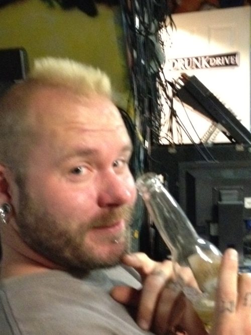 Mohawk-clad brothers kime band member backstage, beer in hand, capturing the raw, unfiltered spirit of recording sessions and DIY music culture.